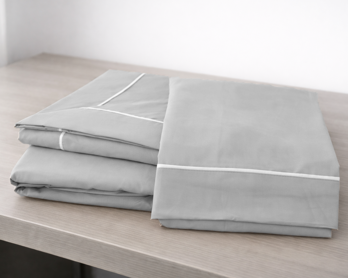 Roupa de cama cinzenta dobrada sobre superfície de madeira clara