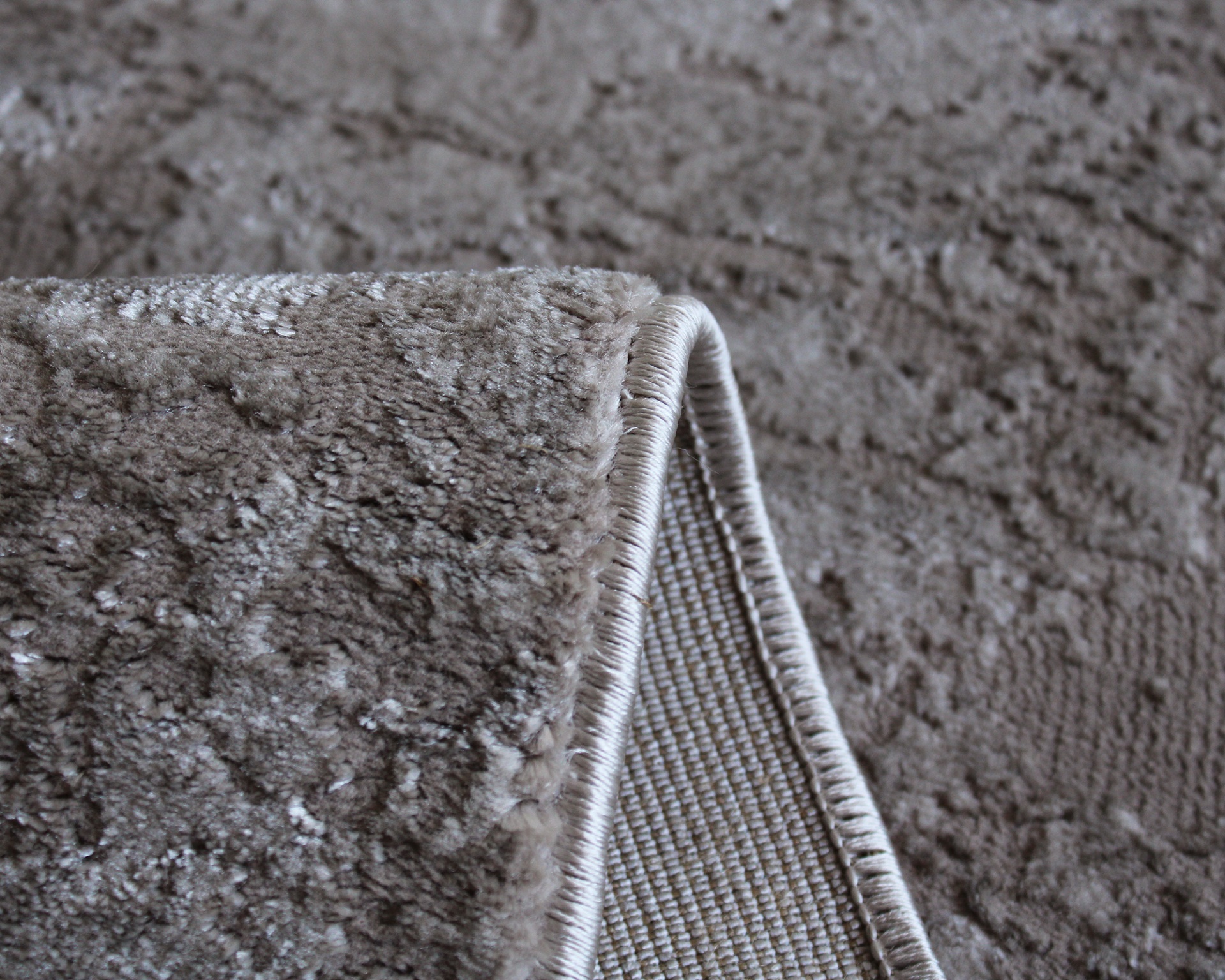 Tapete felpudo castanho claro com padrão em relevo e bordas costuradas.