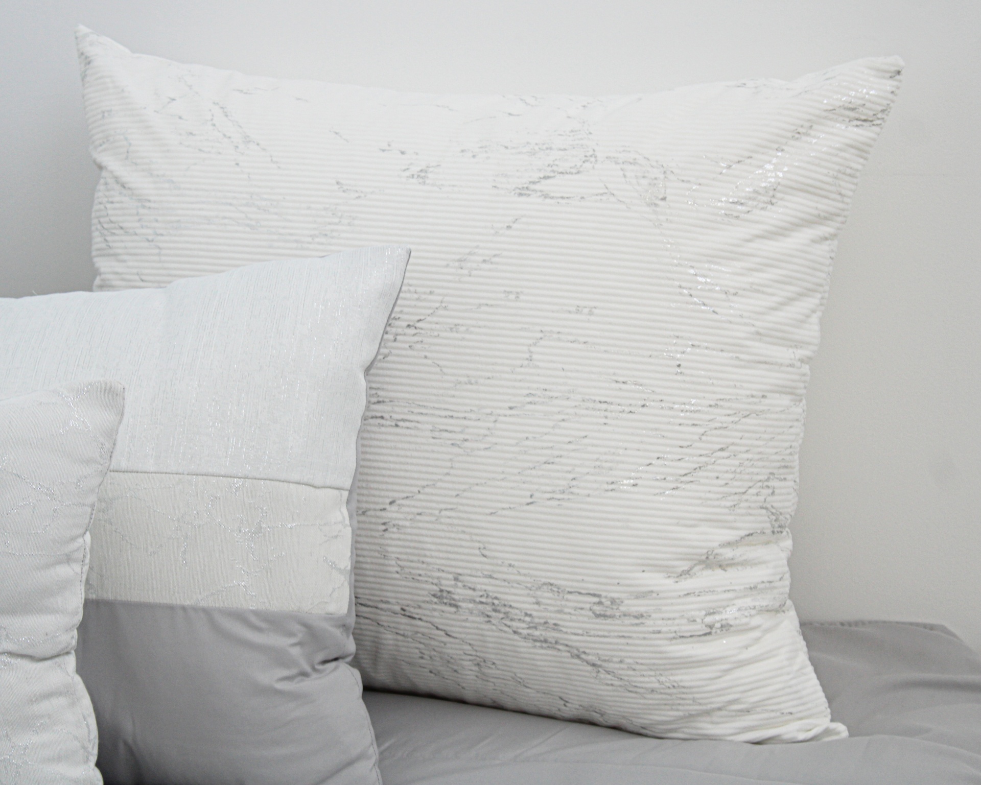 Três almofadas brancas e cinzentas com texturas diferentes sobre superfície cinzenta