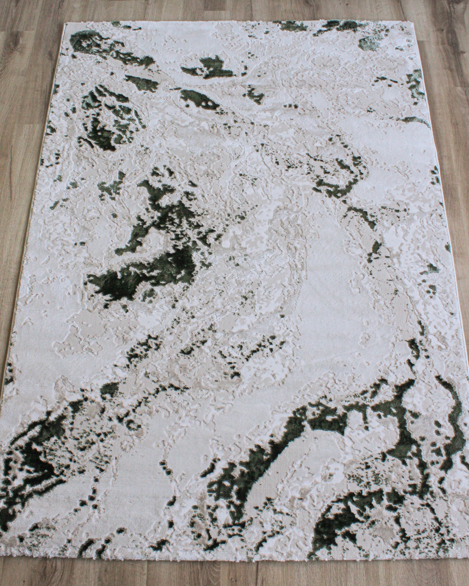 Tapete retangular com padrão abstrato em branco, cinza claro e verde escuro sobre chão de madeira