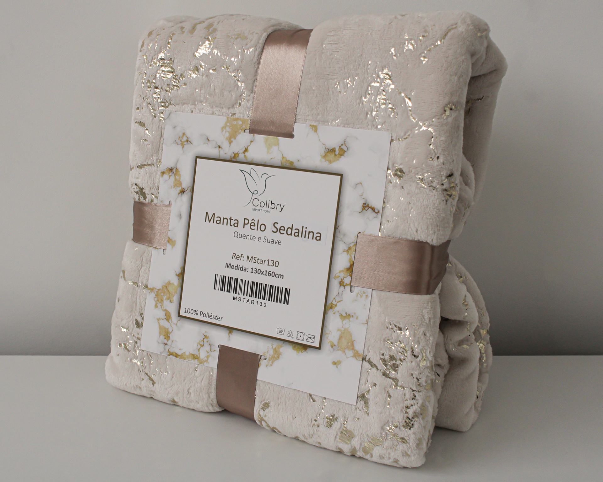 Manta de pelo bege com detalhes dourados, enrolada com fita castanha e etiqueta com texto Colibry Manta Pêlo Sedalina