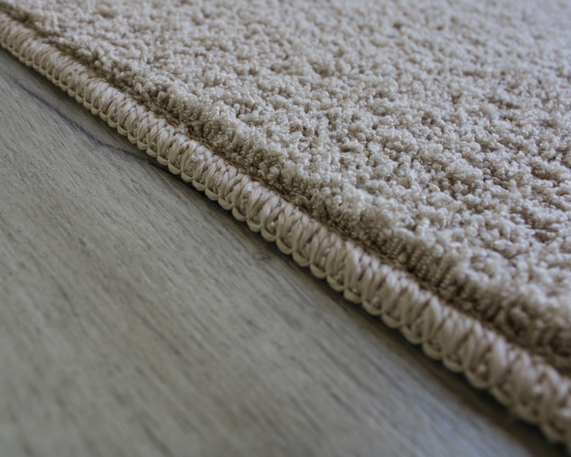 Tapete bege claro com textura de tufos grossos e bordas costuradas numa superfície de madeira clara