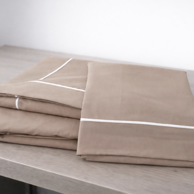 Conjunto de roupa de cama bege com detalhes brancos dobrado sobre mesa de madeira.