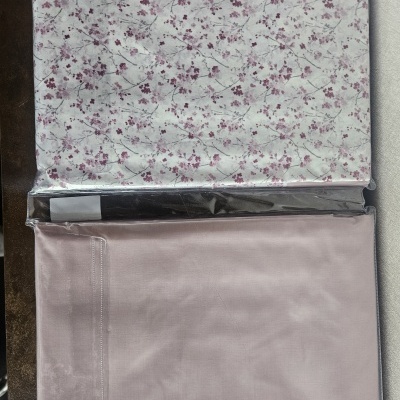 Tecidos dobrados embalados em plástico, um com padrão floral e dois lisos em tons rosa e escuro.