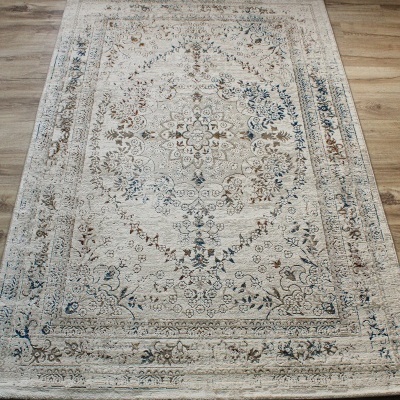 Tapete retangular com padrão floral intricado em tons de bege, azul e castanho sobre chão de madeira.