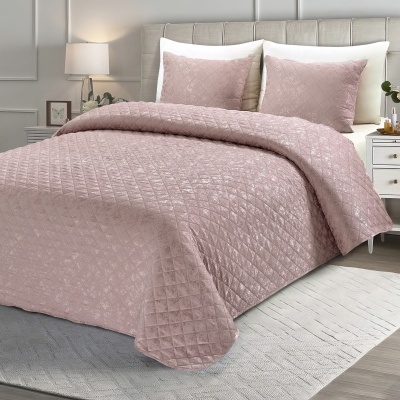 Colcha rosa claro com padrão de losangos numa cama estofada clara, com almofadas, mesas de cabeceira e candeeiros.