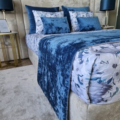 Cama estofada bege com roupa de cama floral azul e branca e almofadas azuis