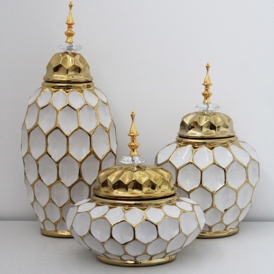 Três frascos decorativos dourados e brancos sobre superfície branca