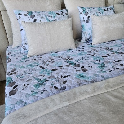 Cama com cabeceira estofada bege, colcha matelassê branca com flores azuis e almofadas bege e estampadas