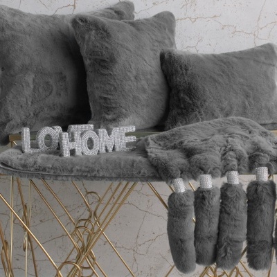 Almofadas e cobertor cinzentos de pelo sobre banco dourado com palavra decorativa LO HOME