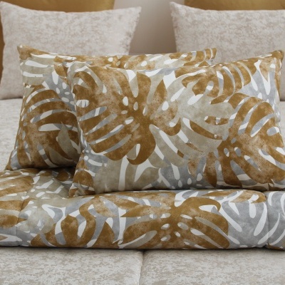 Conjunto de almofadas e edredão com padrão de folhas castanhas e cinzentas sobre cama bege