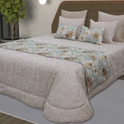 Conjunto de cama com colcha bege, passadeira floral azul e almofadas a combinar.