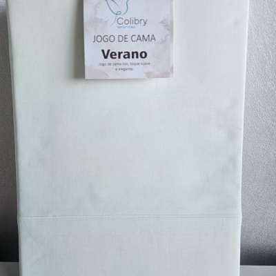 Jogo de cama branco com etiqueta Colibry Verano contra parede cinza