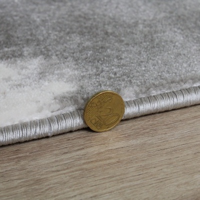 Tapete cinzento com textura suave e moeda dourada sobre chão de madeira.