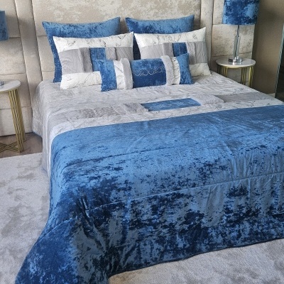 Colcha e almofadas azuis e cinza em cama com cabeceira estofada e mesas de cabeceira