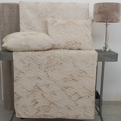 Conjunto de cama bege com padrão marmoreado dourado em mesa cinza com lâmpada