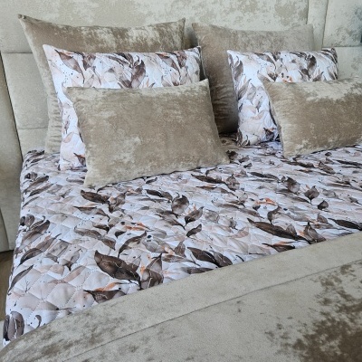 Cama com roupa de cama em padrão de folhas castanhas e almofadas bege aveludadas