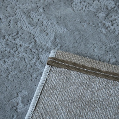 Canto de tapete bege com bordado branco sobre piso cinza texturado