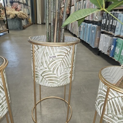 Vaso decorativo metálico dourado com padrão de folhas e preço 34.95€. Loja de decoração ao fundo.