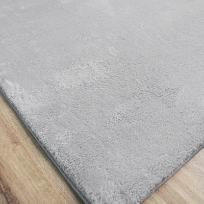 Tapete cinzento claro felpudo sobre chão de madeira clara