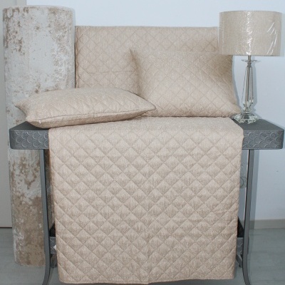 Conjunto de almofadas e manta bege acolchoadas com padrão de quadrados, rolo de tecido e lâmpada de mesa