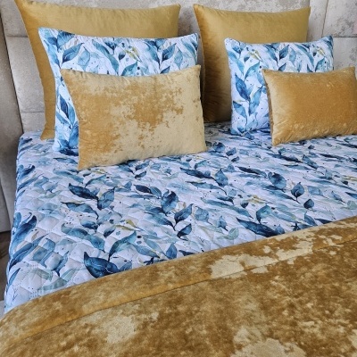 Colcha e almofadas com padrão azul e veludo dourado numa cama com cabeceira cinza