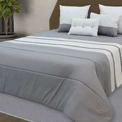 Cama de casal com colcha cinza e almofadas brancas e cinza, tapete cinza e planta em vaso