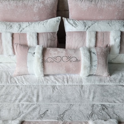 Almofadas decorativas em tons rosa claro e cinza com pelo branco sobre cama cinza