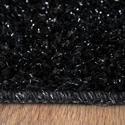 Tapete preto felpudo com borda costurada sobre chão de madeira