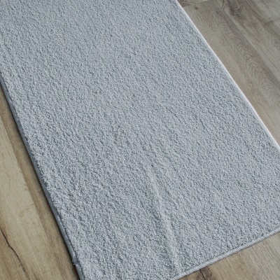 Tapete cinzento claro retangular com textura sobre chão de madeira