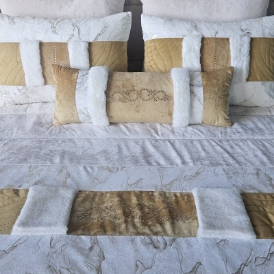 Conjunto de cama em cores bege, dourado e branco com almofadas e edredão texturizados e decorados.