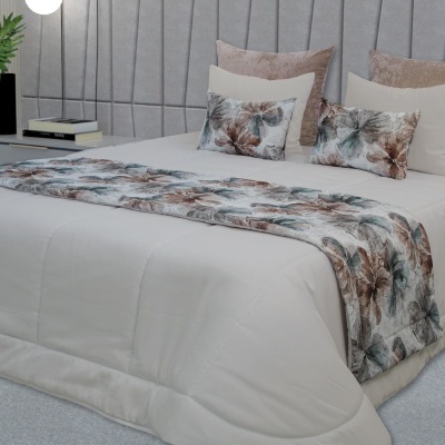 Cama com edredão branco e faixa decorativa floral e almofadas em tons castanhos e bege