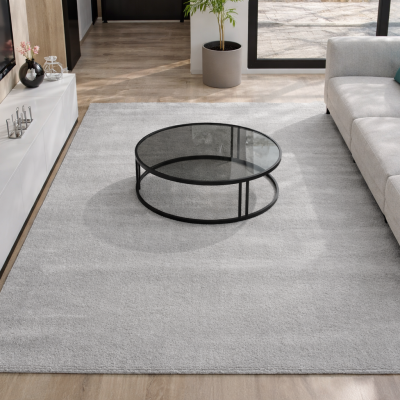 Sala de estar com tapete cinza claro, mesa de centro de vidro e sofá cinza com almofadas coloridas
