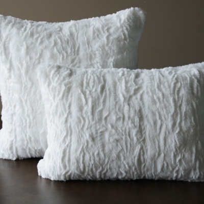 Duas almofadas brancas felpudas, uma quadrada e outra retangular, sobre superfície castanha.