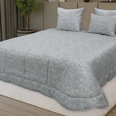 Roupa de cama cinzenta com padrão floral e duas almofadas numa cama com cabeceira bege e planta ao lado