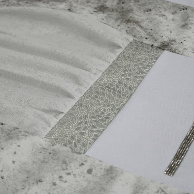 Capa de almofada cinza claro e branca com detalhes texturizados e faixa prateada