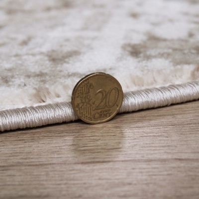 Tapete branco-bege com borda satinada e moeda de 20 euro cêntimos em chão de madeira