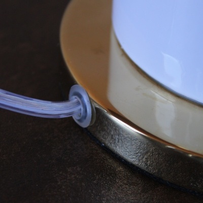 Base dourada de objeto branco com cabo transparente numa superfície preta.