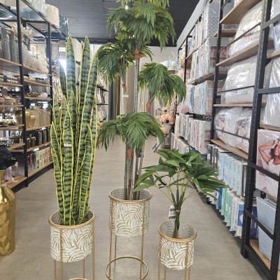 Três vasos com plantas artificiais verdes em ambiente de loja com prateleiras