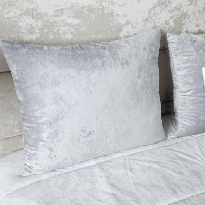 Almofadas e cabeceira de cama cinzenta clara aveludada.