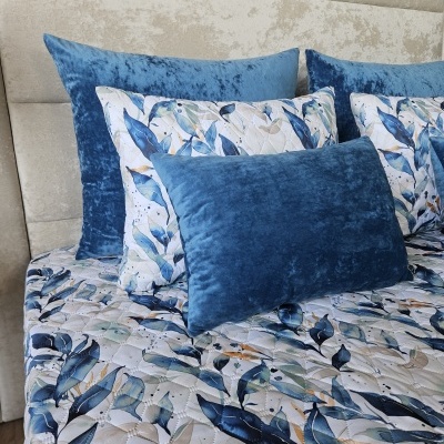 Almofadas e edredão azul floral com almofadas azuis em veludo em cama com cabeceira bege