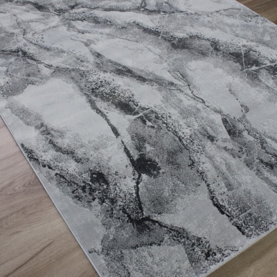 Tapete cinza e preto com padrão abstrato sobre chão de madeira