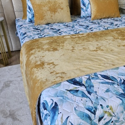 Cama com colcha e almofadas decorativas em tons azul, verde e amarelo mostarda