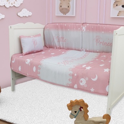 Cama de criança branca com roupa de cama rosa e cinza e almofada prateada num quarto rosa com brinquedos