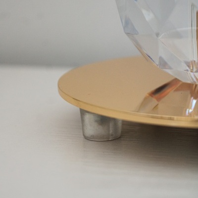 Base dourada metálica com apoio cinzento e objeto facetado transparente