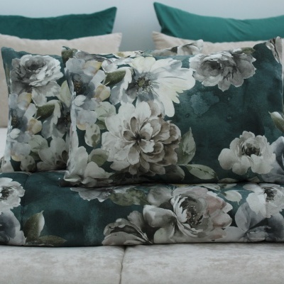 Almofadas e manta com padrão floral verde e branco sobre cama com almofadas lisas