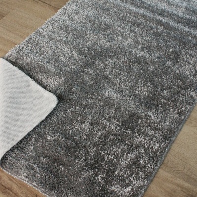 Tapete cinza felpudo com base branca antiderrapante sobre chão de madeira