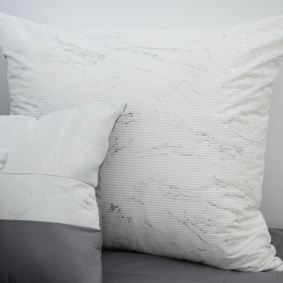 Três almofadas decorativas brancas e cinzentas sobre superfície cinzenta