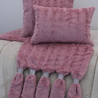 Almofadas e manta rosa felpudo com franjas prateadas sobre sofá cinzento