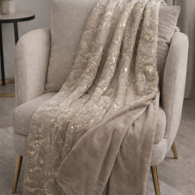 Manta bege com padrão dourado sobre cadeira creme com pernas douradas